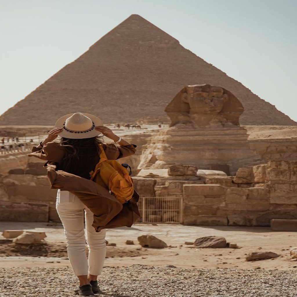 A female traveler wearing a sun hat and yellow backpack looks at the Great Pyramid of Giza and the Sphinx, a highlight of 11-day Egypt tour packages.