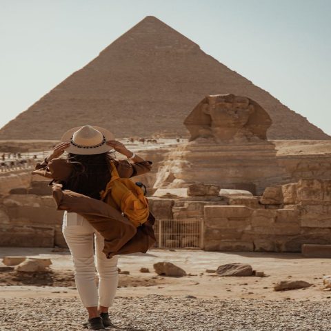 A female traveler wearing a sun hat and yellow backpack looks at the Great Pyramid of Giza and the Sphinx, a highlight of 11-day Egypt tour packages.