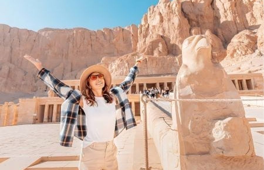 Happy tourist posing with open arms in front of the Horus statue at Hatshepsut Temple during an 11 day christmas egypt tour cairo nile cruise hurghada
