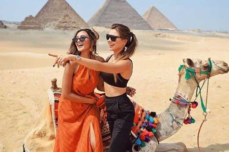 Two Women Smiling Next To A Camel With The Pyramids Of Giza In The Background During An 11 Day Cairo Nile Cruise Alexandria Tour.