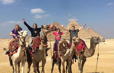 Happy travelers enjoying a camel ride during an 11 day luxury egypt escorted tour from usa with the Giza Pyramids in the background