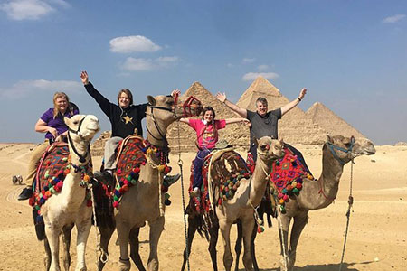Happy travelers enjoying a camel ride during an 11 day luxury egypt escorted tour from usa with the Giza Pyramids in the background
