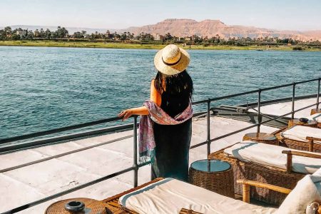 a woman standing on a deck of nile cruise Aswan to Luxor overlooking a body of water