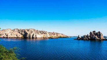 A stunning panoramic view of Lake Nasser, showcasing its serene blue waters against the vast desert backdrop and ancient ruins nearby.
