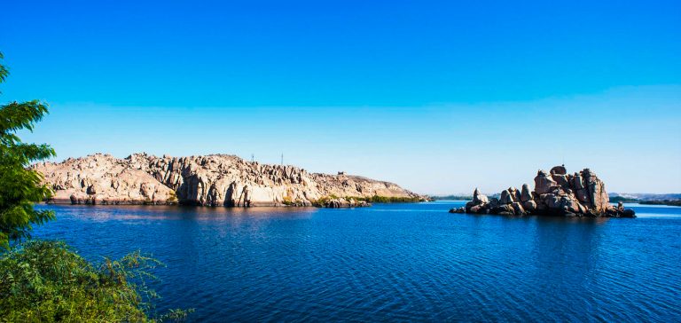 A stunning panoramic view of Lake Nasser, showcasing its serene blue waters against the vast desert backdrop and ancient ruins nearby.