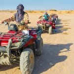 Desert safari on quad bikes across, sandy desert landscape under a clear blue sky.