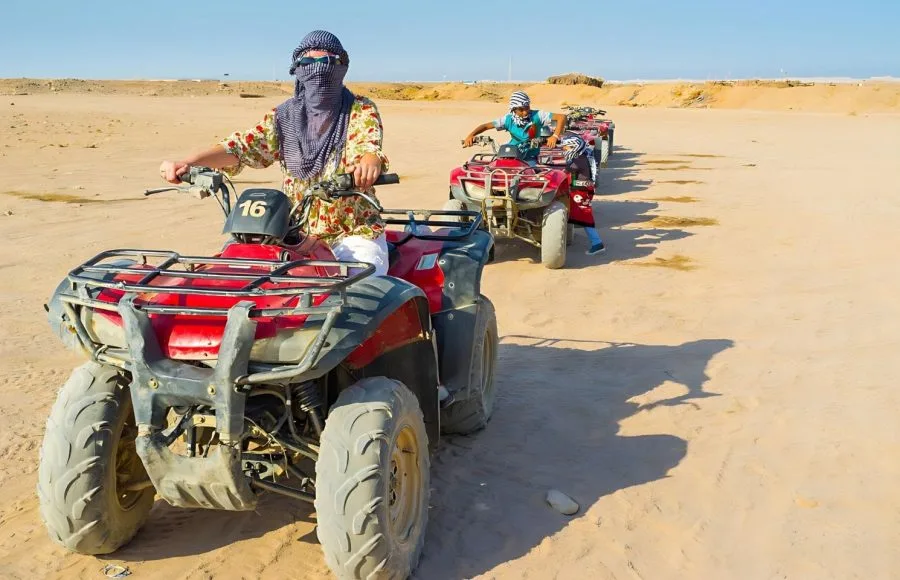 Desert safari on quad bikes across, sandy desert landscape under a clear blue sky.