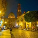 Al Muizz Street in Old Cairo at night, illuminated by yellow streetlights, with historic buildings.