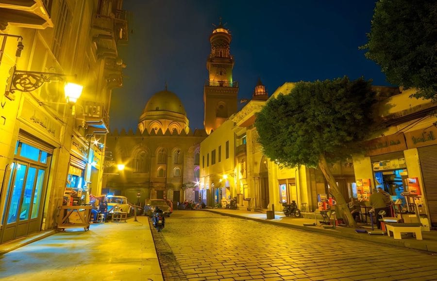 Al Muizz Street in Old Cairo at night, illuminated by yellow streetlights, with historic buildings.