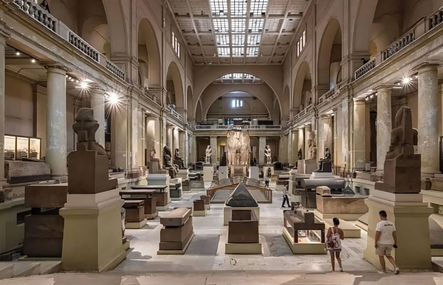 Large stone statues and sarcophagi displayed in the grand central hall of the Egyptian Museum in Cairo.