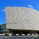The large, curved granite facade of the Bibliotheca Alexandrina in Egypt, covered in carved hieroglyphic-like characters, seen during a daylight Trip.
