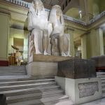 A monumental, seated Colossal Statue of Pharoah Amenhotep III and Queen Tiye at the Egyptian Museum, Cairo, made of white quartzite and displayed at the top of a grand staircase.