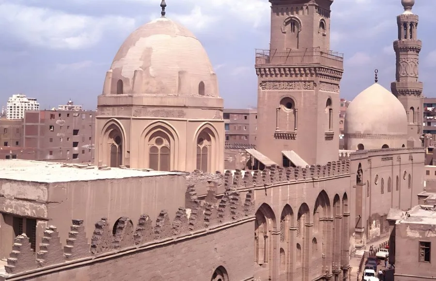 An exterior view of the Complex of Sultan Qalawun in Islamic Cairo, featuring its impressive dome, minarets, and crenelated walls.