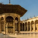 The large, sunlit Courtyard of Mosque of Muhammad Ali inside the Citadel in Cairo, featuring the elaborate central ablutions fountain and surrounding arched porticos.