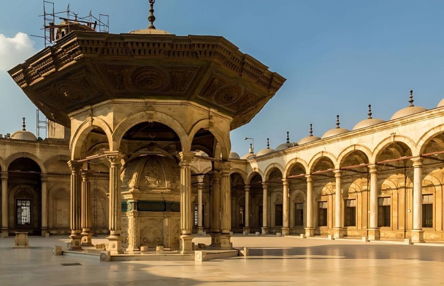 The large, sunlit Courtyard of Mosque of Muhammad Ali inside the Citadel in Cairo, featuring the elaborate central ablutions fountain and surrounding arched porticos.