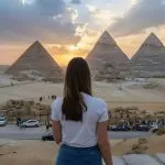 A Female Traveler views the Pyramids of Giza at sunset during a 5 Days Cairo Alexandria Tour, showcasing the pyramids and surrounding desert landscape.