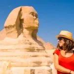 Female tourist in a hat smiling next to the colossal Great Sphinx of Giza Egypt landmark