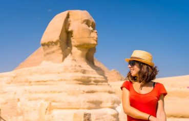 Female tourist in a hat smiling next to the colossal Great Sphinx of Giza Egypt landmark