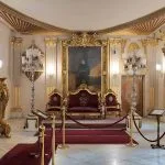 The opulent and highly gilded Hall at Manial Palace of Prince Mohammed Ali, featuring a central portrait, velvet seating, and elaborate chandeliers.