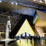 The Grand Egyptian Museum (GEM) welcomes visitors with its spacious, modern interior, featuring a towering statue, and groups of people exploring and enjoying the space.