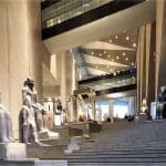 Rows of ancient stone statues of pharaohs and deities displayed on modern steps in the grand, light-filled atrium Inside Grand Egyptian Museum Giza.