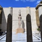 A statue of a draped female figure topped with a modius (headdress) stands in a sunlit courtyard between massive stone columns, showcasing an exhibit Inside Greco-Roman Museum.