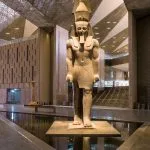 A colossal statue of Ramesses II stands on a podium in the modern, expansive atrium of the Inside The Grand Egyptian Museum GEM, surrounded by sleek architecture and reflective floors.