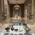 The elegant interior gallery of the Islamic art Museum in Cairo, featuring vaulted arches, and displays of ceramics and metalwork artifacts in glass cases.