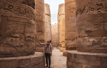 A person looking up at the intricately carved columns of the Karnak Temple's Hypostyle Hall.