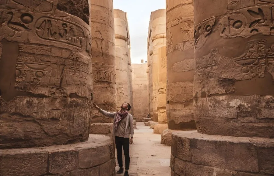A person looking up at the intricately carved columns of the Karnak Temple's Hypostyle Hall.