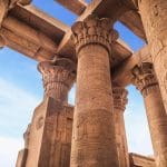 Ornate columns of Karnak Temple's Hypostyle Hall against a blue sky.