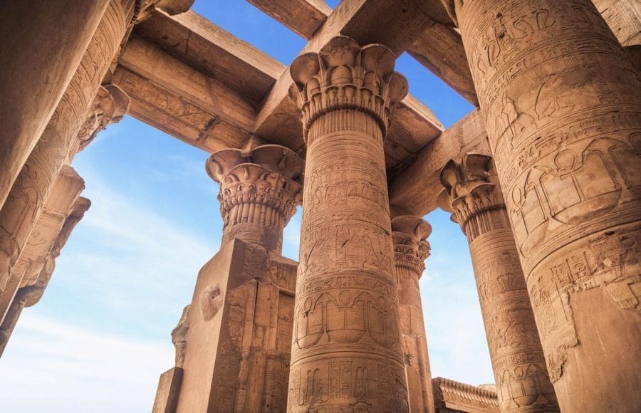 Ornate columns of Karnak Temple's Hypostyle Hall against a blue sky.