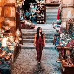 A woman strolls through Cairo's lively Khan El Khalili Bazaar, surrounded by vibrant stalls of lamps, textiles, and traditional goods.