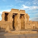 a stone building with pillars with Temple of Kom Ombo in the background