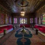 The opulent reception hall Manial Palace of Prince Mohammed Ali, featuring richly decorated ceilings, colorful stained-glass windows, plush red velvet seating, and oriental carpets.