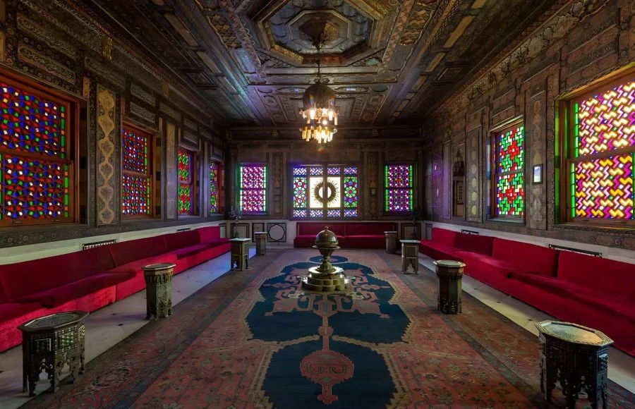 The opulent reception hall Manial Palace of Prince Mohammed Ali, featuring richly decorated ceilings, colorful stained-glass windows, plush red velvet seating, and oriental carpets.