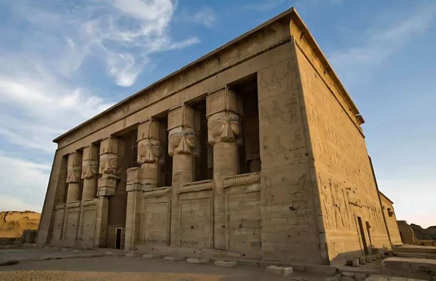 A wide shot of the majestic Ptolemaic Temple of Hathor at Dendera, featuring large columns with Hathoric capitals under a bright sky.