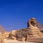 Great Sphinx of Giza and ancient Egyptian pyramids towering under a bright blue sky in the historic Giza Necropolis.