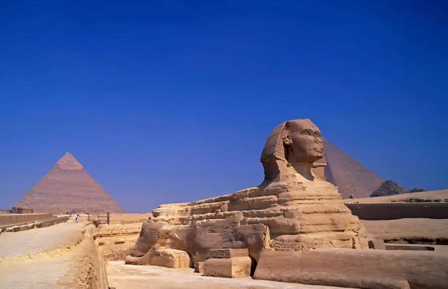 Great Sphinx of Giza and ancient Egyptian pyramids towering under a bright blue sky in the historic Giza Necropolis.