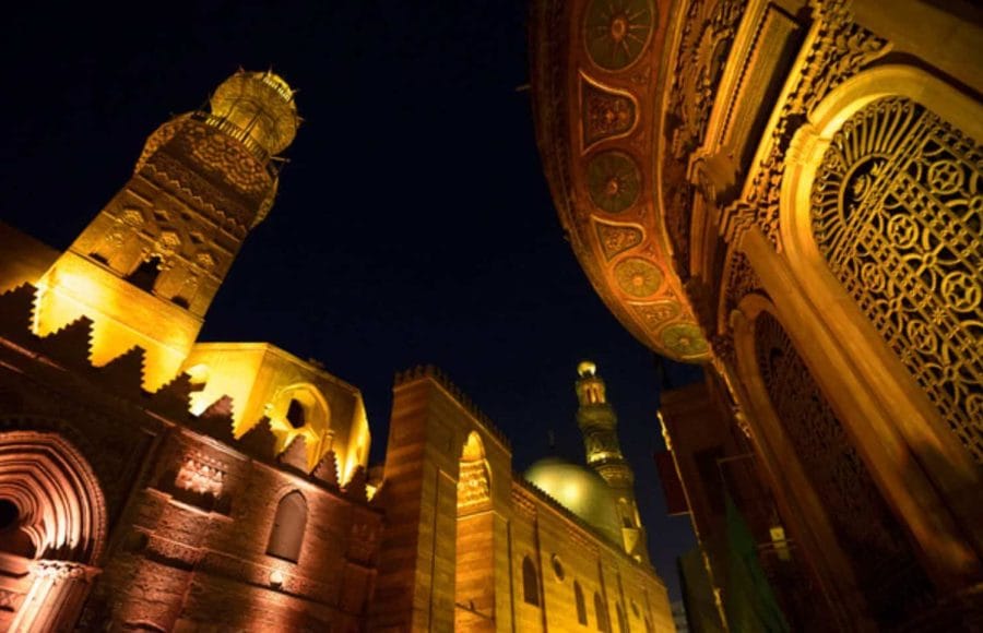 The illuminated minaret and ornate architecture of the Qalawun Complex at night in Islamic Cairo.