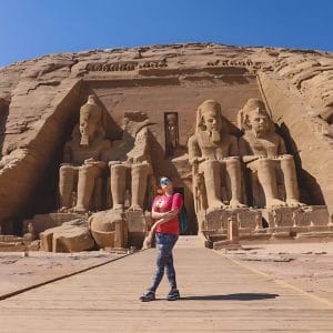 A Solo Woman in front of the Colossal Statues of Ramesses ii Abu Simbel, standing on a wooden walkway facing the four massive seated figures carved into the mountain facade of the Great Temple.