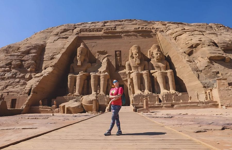 A Solo Woman in front of the Colossal Statues of Ramesses ii Abu Simbel, standing on a wooden walkway facing the four massive seated figures carved into the mountain facade of the Great Temple.