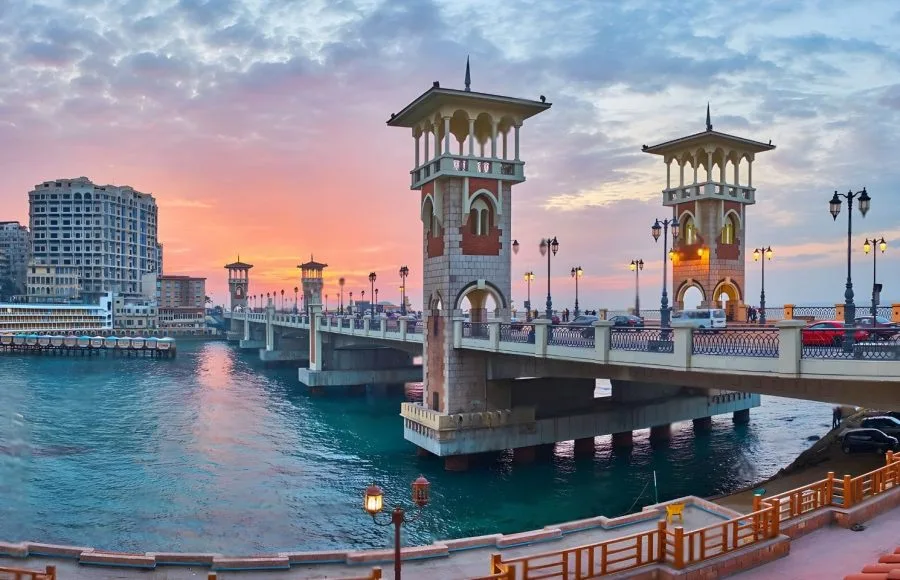 The Stanley Bridge Alexandrina Trip at sunset, showing the ornate towers and structure arching over the turquoise sea, connecting the coastline of Alexandria.