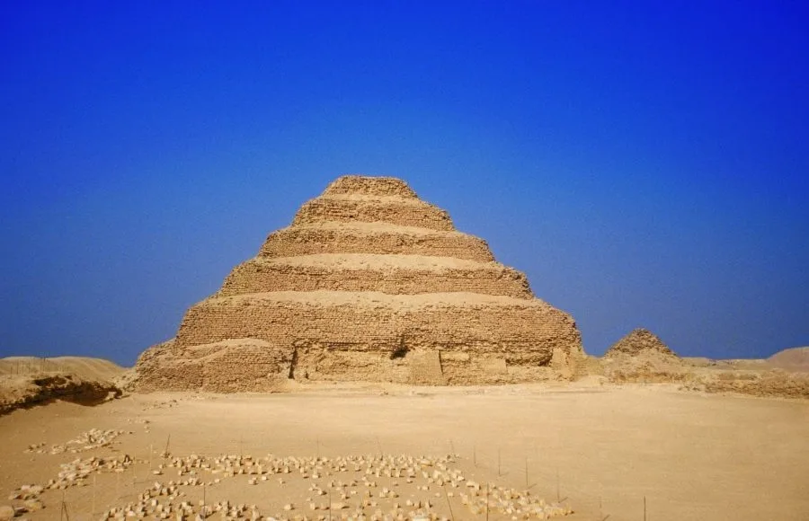 The ancient, weathered stone steps of the Step Pyramids Saqqara Necropolis, the massive structure rising against a clear blue sky in the desert landscape.