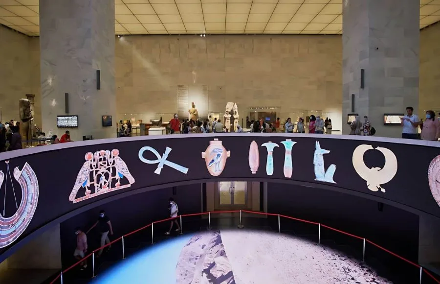 The interior of the National Museum of Egyptian Civilization (NMEC) with a large circular display featuring illuminated ancient Egyptian symbols and hieroglyphs.