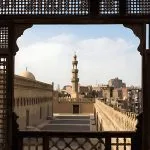 A view of the rooftops and minaret of the Mosque of Ibn Tulun in Cairo, framed by the traditional wooden lattice screen (mashrabiya) from The Roof Terrace of the Gayer Anderson Museum Cairo.