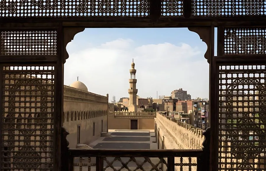 A view of the rooftops and minaret of the Mosque of Ibn Tulun in Cairo, framed by the traditional wooden lattice screen (mashrabiya) from The Roof Terrace of the Gayer Anderson Museum Cairo.