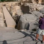 A tourist takes a picture of the Unfinished Obelisk, still embedded in the granite quarry, showing a massive, partially carved stone monument.