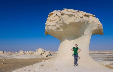 Tourist standing next to a large, white chalk mushroom rock formation in the White Desert, Egypt.