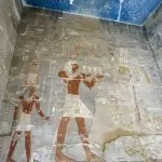 A detailed view of the colorful, well-preserved tomb paintings and hieroglyphs on a wall inside a tomb within the Valley of the Kings Luxor.